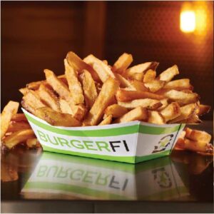 A close-up of a large serving of golden-brown french fries in a white and green paper container with the BurgerFi logo. The fries look perfectly cooked and crispy.