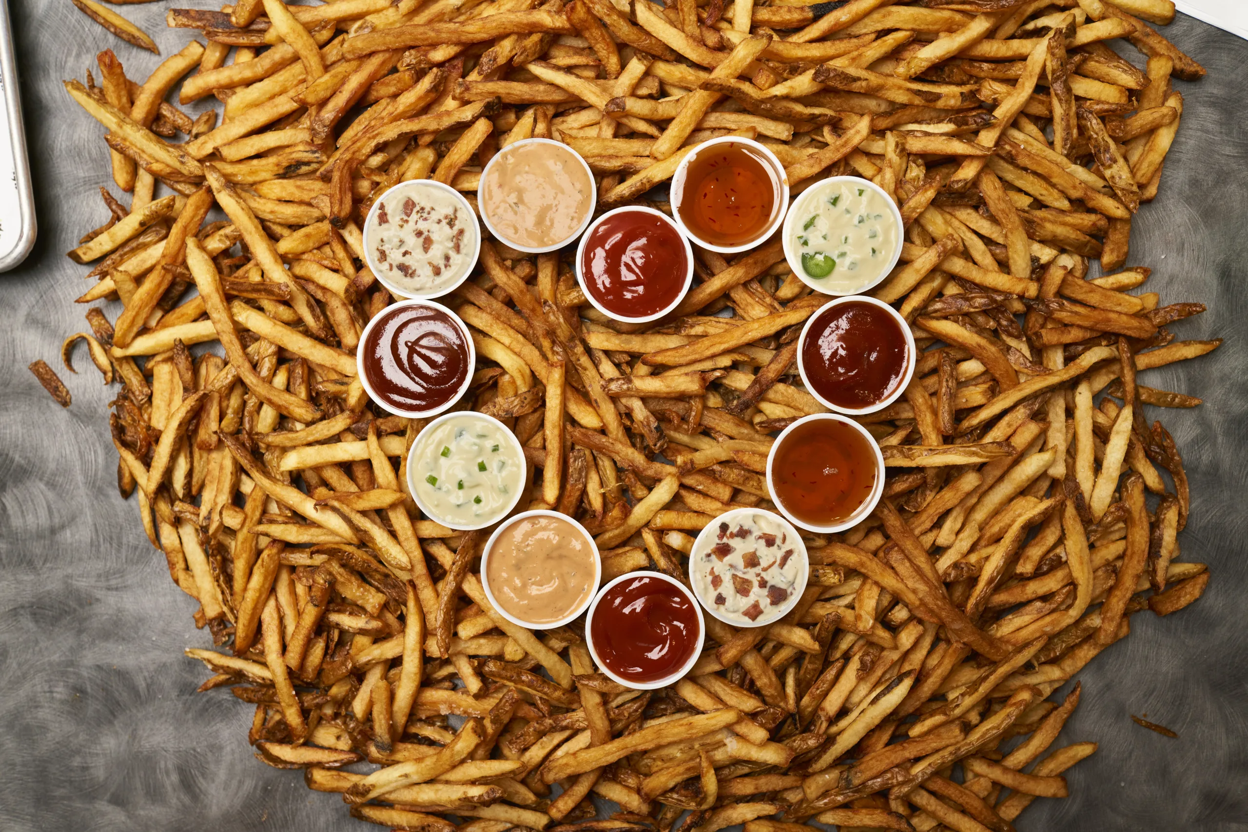 A heart-shaped arrangement of french fries with a variety of dipping sauces, perfect for sharing with friends and family.