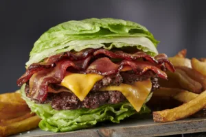 Lettuce-wrapped BurgerFi burger featuring crispy bacon, melted cheese, and juicy patties, served with a side of golden fries.