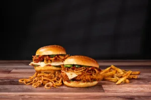 Two chicken sandwiches with crispy onions, cheese, and pickles on buns, served with a side of french fries.