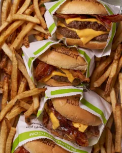 A double cheeseburger with two beef patties, cheese, bacon, and lettuce on a bun, served with a side of french fries.