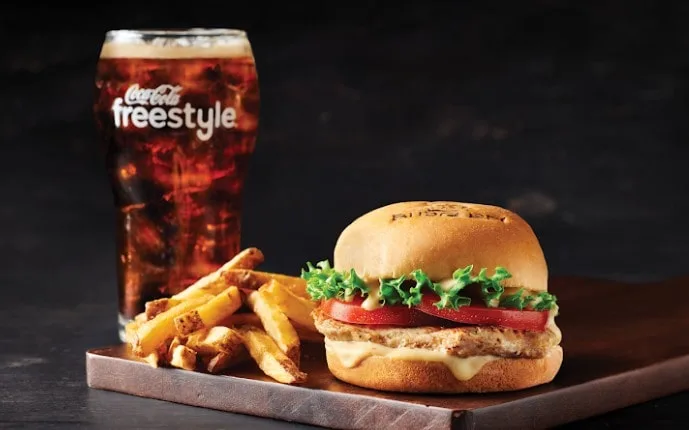 A delicious plate of burgers and fries with a refreshing Coca-Cola Freestyle.