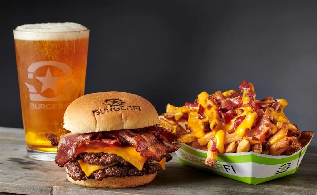 A juicy burger stacked high with cheese and bacon, served alongside a generous portion of crispy fries and a frosty glass of beer.