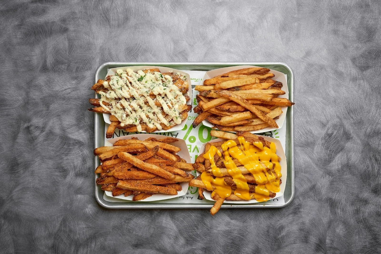 A variety of loaded fries on a tray, including chili cheese fries, garlic parmesan fries, and more.