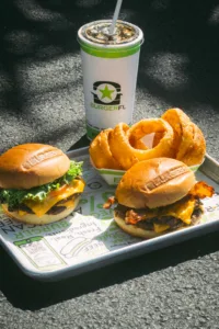 A tray of food with two burgers, onion rings, and a drink.