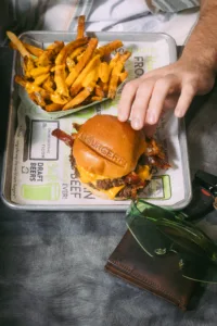 A close-up photo of a juicy burger topped with melted cheese and crispy bacon, served alongside a generous portion of golden french fries. 