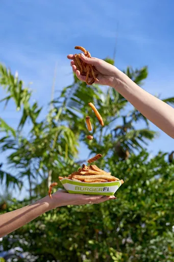 A hand holding up crispy French fries from BurgerFi