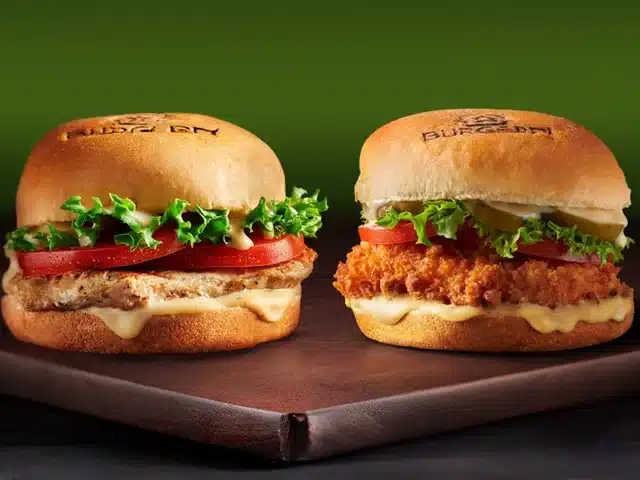 Two delicious BurgerFi chicken sandwiches with fresh lettuce, tomato, and melted cheese on a wooden board.